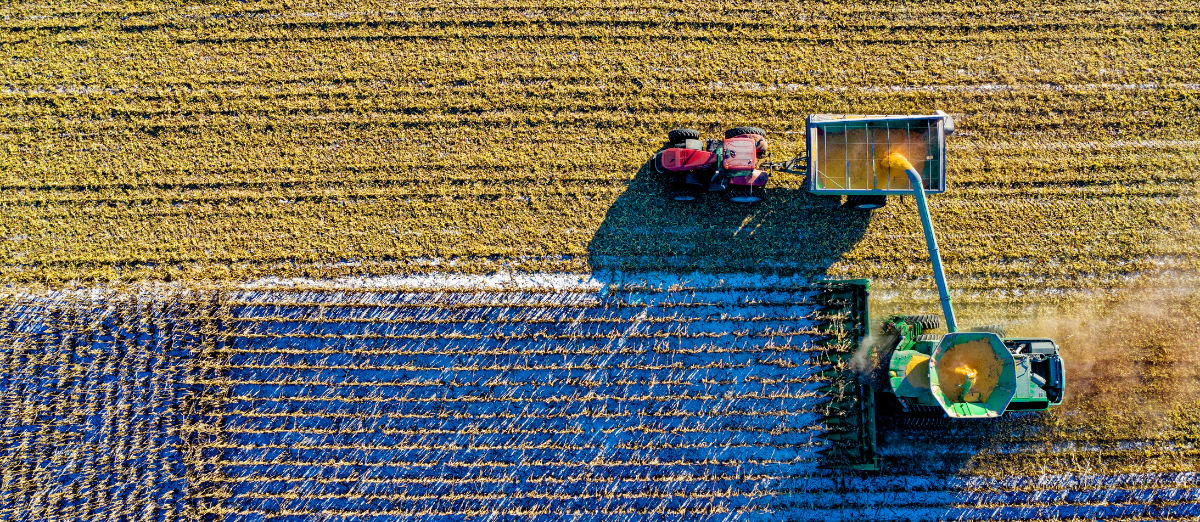 overhead picture of a harvester and a tractor pulling a grain bin driving across a field working together